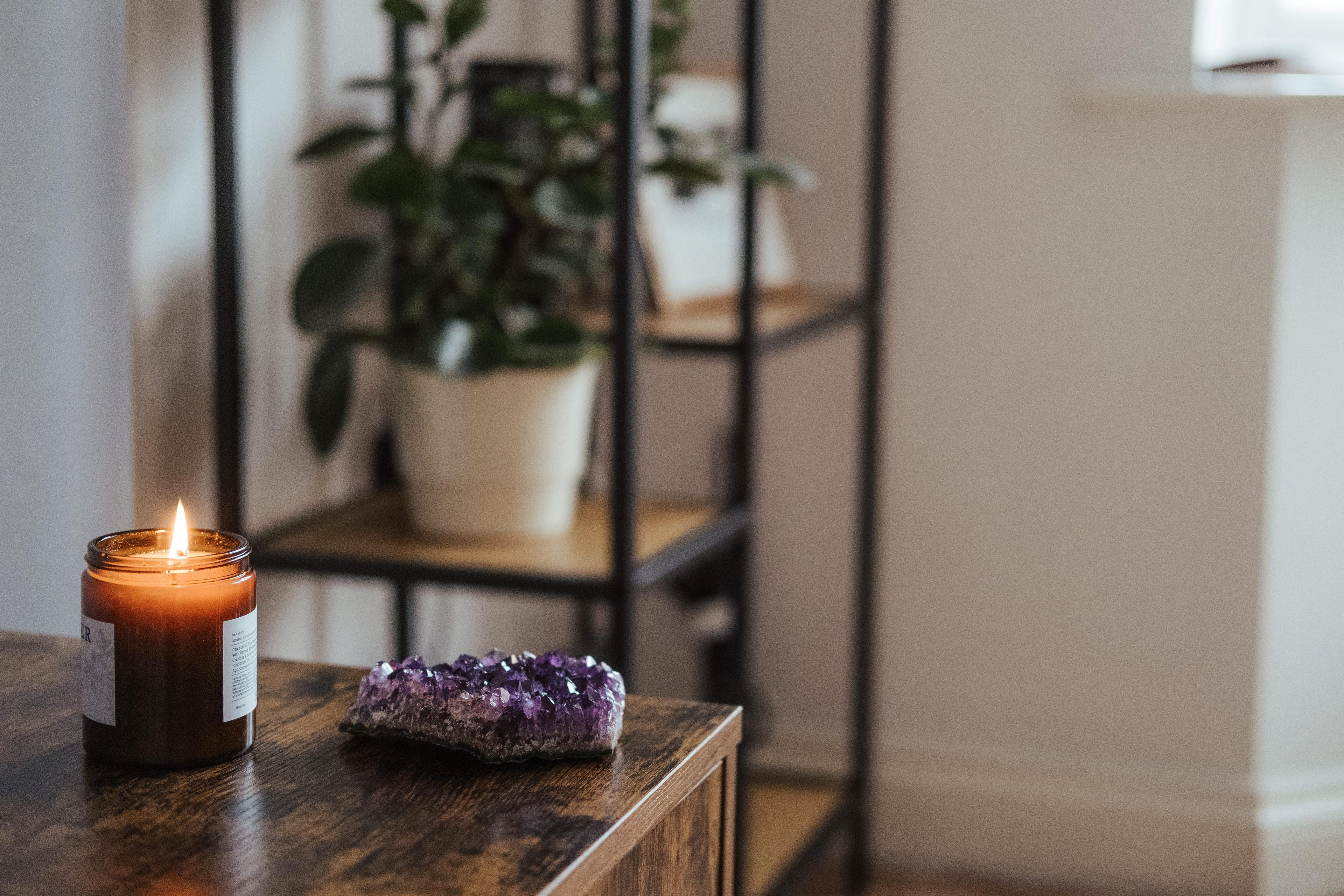 candle burning with a chunk of amethyst next to it and a plant shelf in the background
