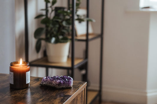 candle burning with a chunk of amethyst next to it and a plant shelf in the background