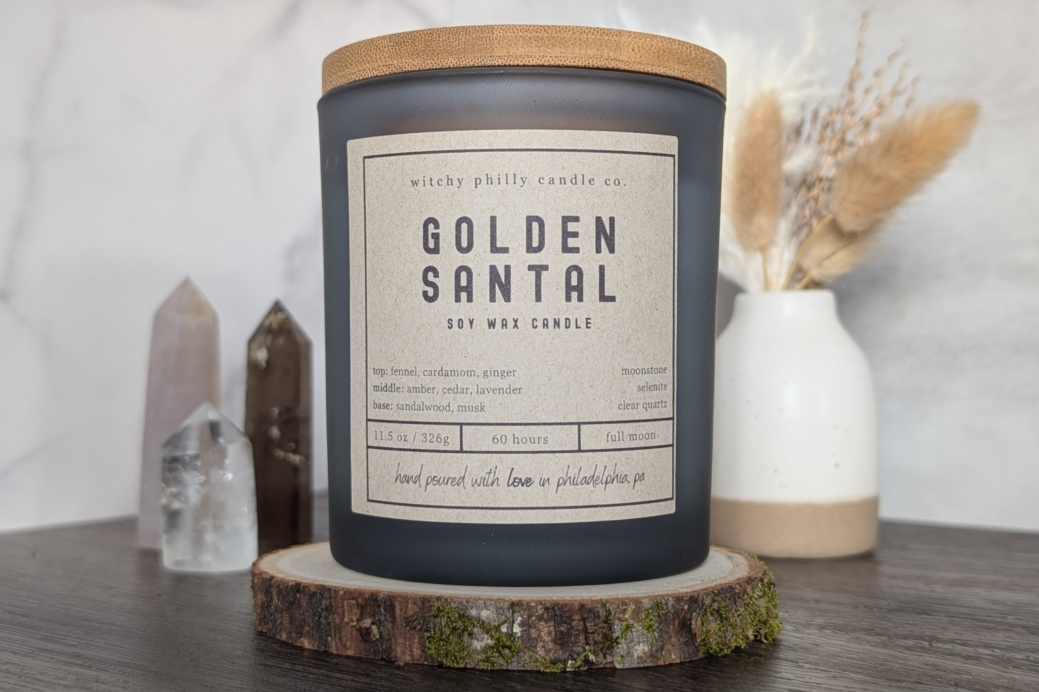 golden santal candle on a wood slice with crystals and pampas grass in the background