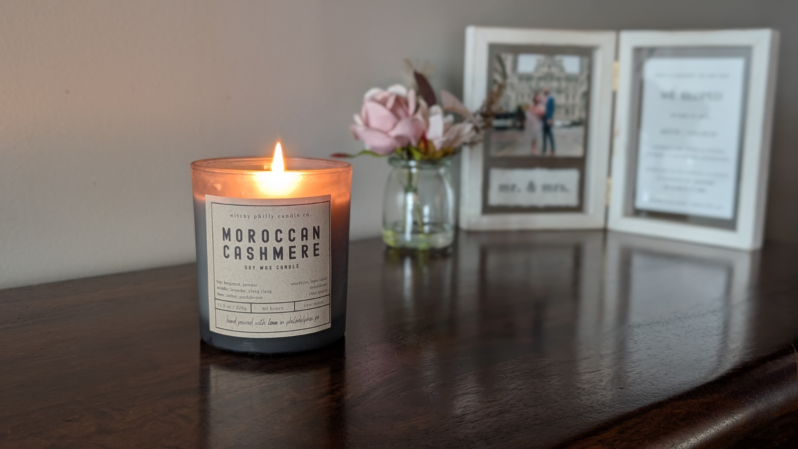 moroccan cashmere candle on a table with a picture frame and roses in the background